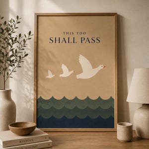 以下が含まれることがあります： 「THIS TOO SHALL PASS」の文字と、青と緑の波の上を飛ぶ3羽の白い鳥のグラフィックが描かれた、額装されたアートプリント。 アートワークはニュートラルな色使いで、木製のフレームに入っています。