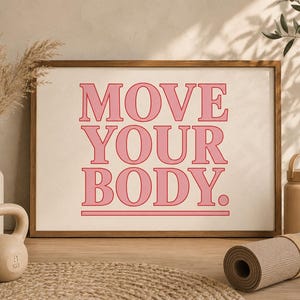 May include: A framed print with the words "MOVE YOUR BODY" in pink letters. A beige kettlebell, a water bottle, and a rolled-up yoga mat are on a wooden surface. A vase with dried plants is on the left.