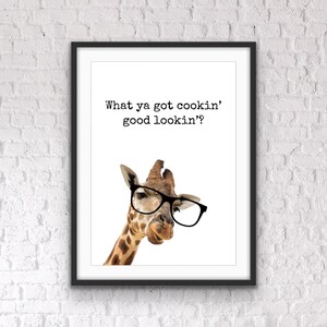 May include: Framed art print featuring a giraffe wearing black glasses. The giraffe is brown and white with a long neck. The print has the text "What ya got cookin' good lookin'?" in black font on a white background.