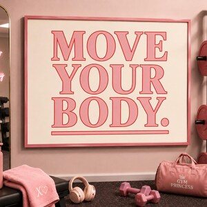 May include: Pink framed wall art with the words "MOVE YOUR BODY" in a bold font. A pink water bottle, towel, headphones, dumbbells, and a gym bag are in the foreground. A mirror and weight rack are in the background.