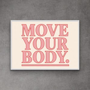 May include: A framed print with the words "MOVE YOUR BODY" in a bold, pink font. The text is centered on a cream-colored background, with a pink line beneath the words. The frame is white, and the overall aesthetic is modern and motivational.