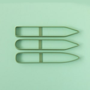 Pode incluir: Três cortadores de biscoitos em forma de lápis de plástico verde sobre um fundo verde claro.