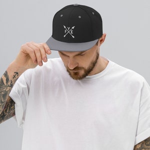 May include: A black and grey baseball cap with a white embroidered logo that says "FYE" with two crossed arrows.