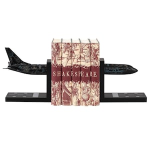 Op de afbeelding: Een zwarte vliegtuigboekensteun met een set van vijf rode en crèmekleurige boeken met het woord "SHAKESPEARE" op de rug.