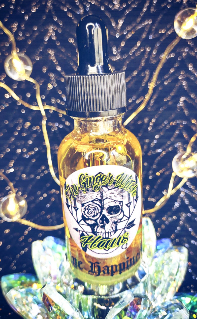 May include: A clear glass bottle with a black dropper top and a yellow liquid inside. The bottle has a label with the text "The Ginger Witch Haus" and "The Happiness" in a black and yellow font.