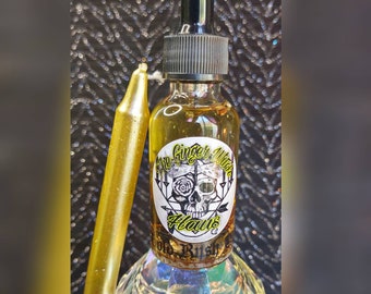 May include: A glass bottle with a black dropper top and a yellow label that reads "The Ginger Witch Haus Gold Rush". The label features a skull with a rose and an arrow design. The bottle is filled with a clear, golden liquid.