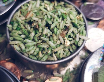 May include: A small metal container filled with green and gold rice. The rice is sprinkled with gold flakes and has a speckled green appearance.