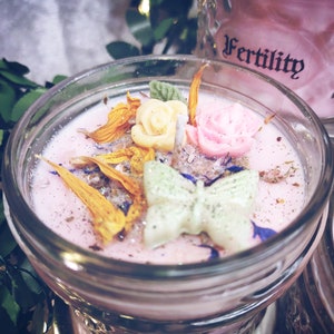 May include: Pink candle in a glass jar with a butterfly, flowers, and glitter. The jar has the word "Fertility" written on it.