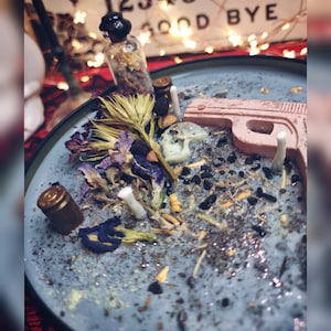 May include: A blue plate with a pink gun-shaped candle, dried flowers, and small glass bottles. The plate is covered in black and gold glitter.