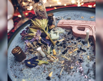 May include: A blue plate with a pink gun-shaped candle, dried flowers, and small glass bottles. The plate is covered in black and gold glitter.