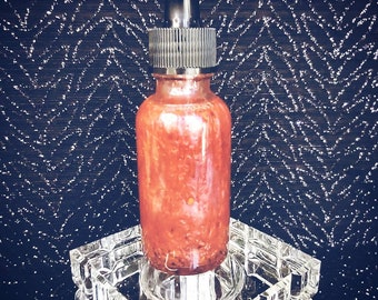 May include: A clear glass bottle with a black dropper top filled with a red liquid. The bottle is sitting on a clear glass stand.