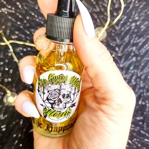 May include: A clear glass bottle with a black dropper top and a yellow label. The label features a skull with a rose and the text "The Ginger Witch Haunts The Happiness".