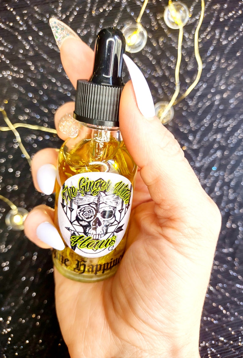 May include: A clear glass bottle with a black dropper top and a yellow label. The label features a skull with a rose and the text "The Ginger Witch Haunts The Happiness".