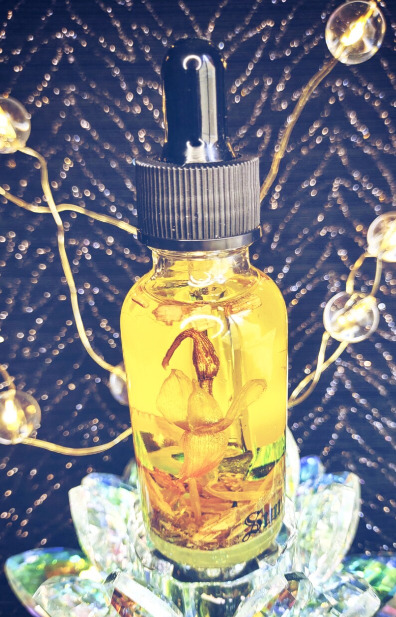 May include: A clear glass bottle with a black dropper top filled with a yellow liquid and a dried flower inside. The bottle is sitting on a clear glass base.