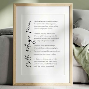 May include: A framed print featuring a poem titled "Cello Player Poem" in elegant script. The poem is printed on a white background, framed by a light wood frame. The artwork is displayed on a bed with pillows and a green blanket.