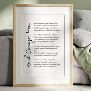 Può includere: Una stampa incorniciata con la "Land Surveyor Poem" in elegante scrittura. La poesia è centrata su uno sfondo bianco, racchiusa in una cornice di legno chiaro. L'opera d'arte è esposta su un divano dai toni neutri, creando un'estetica semplice ma sofisticata.