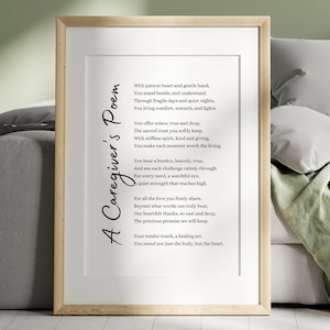 May include: A framed print featuring a poem titled "A Caregiver's Poem." The poem is in black script on a white background, framed in a light wood frame. The print is displayed on a bed with pillows and a blanket.