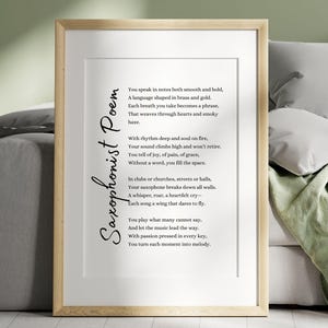 May include: A framed print featuring a poem titled "Saxophonist Poem." The text is in black on a white background, with a wooden frame. The poem's title is written vertically on the left side. The frame is displayed on a bed.