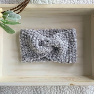 May include: A grey, fuzzy, knotted headband in a white wooden tray.
