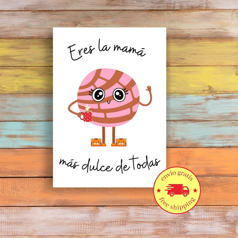 May include: A white card with a cartoon concha pastry character with a smiling face, holding a coffee cup. The text "Eres la mam&aacute; m&aacute;s dulce de todas" is written above and below the character. The background is a colorful wooden surface.