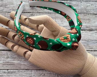 May include: Green headband with a white background and a pattern of brown and white cookies with white hearts. The headband is tied in a knot.