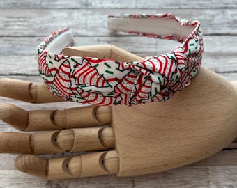 May include: A white headband with a red and green Christmas tree pattern. The headband is knotted on top.