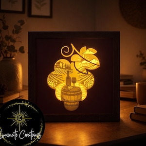 May include: A framed, illuminated art piece with a grape cluster design. The artwork shows a vineyard scene with a wine bottle, glass, and barrel. The frame is dark brown, and the light emits a warm glow. The artwork is on a wooden table.