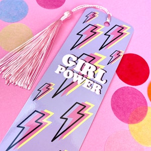 May include: A purple bookmark with a pink tassel. The bookmark has a pattern of yellow and pink lightning bolts and the words "GIRL POWER" in white letters.
