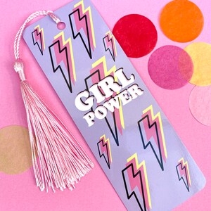 May include: Purple bookmark with a pink and yellow lightning bolt pattern and the text "GIRL POWER" in white letters. The bookmark has a pink tassel.