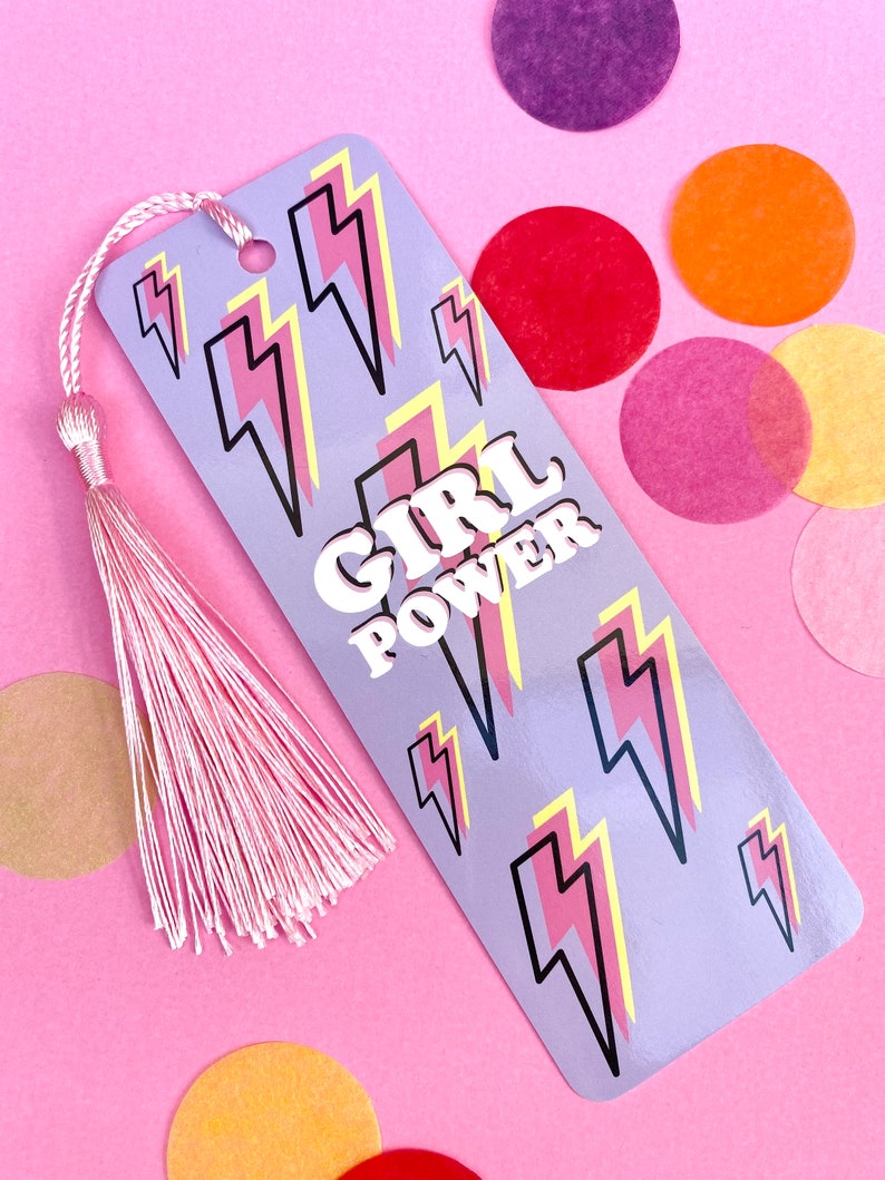 May include: Purple bookmark with a pink and yellow lightning bolt pattern and the text "GIRL POWER" in white letters. The bookmark has a pink tassel.