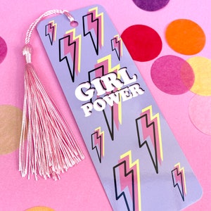 May include: A purple bookmark with a pink tassel. The bookmark has a pattern of yellow and pink lightning bolts and the text "GIRL POWER" in white letters.