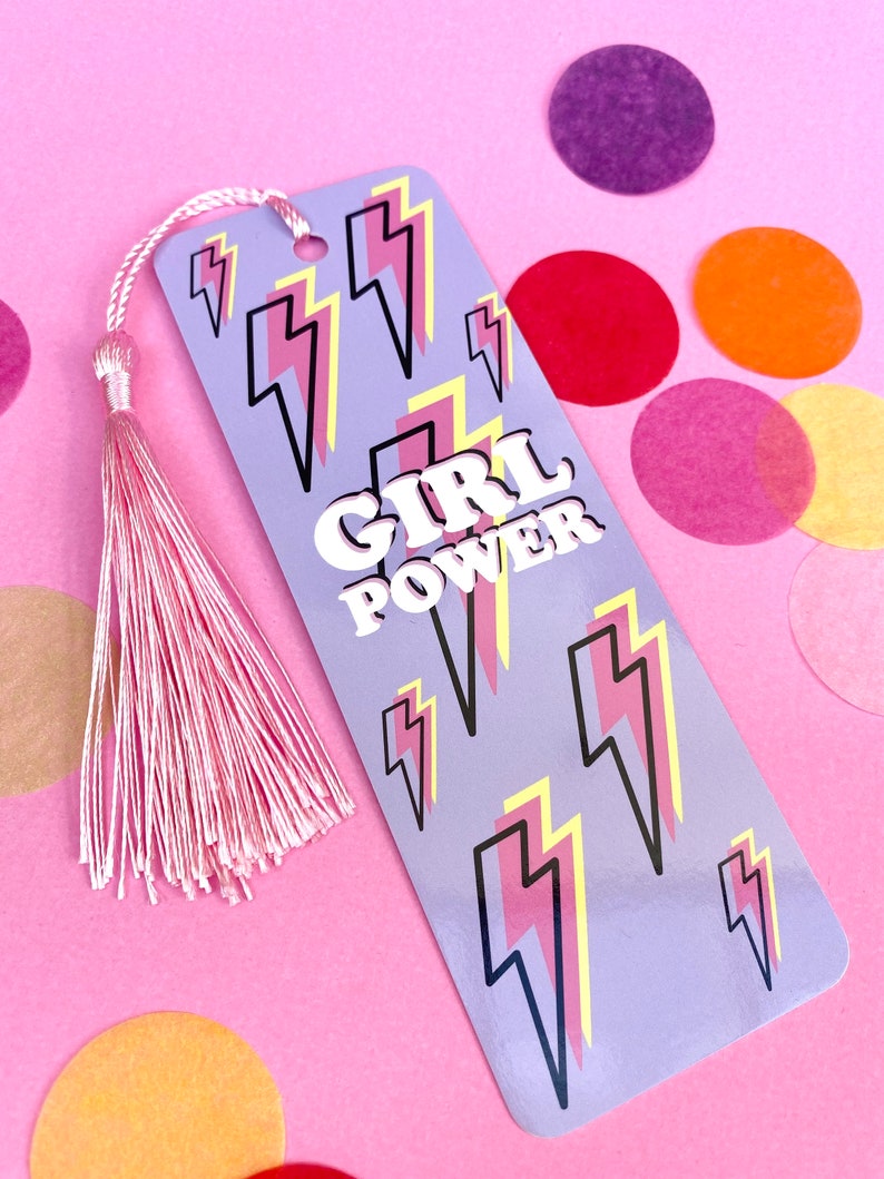 May include: A purple bookmark with a pink tassel. The bookmark has a pattern of yellow and pink lightning bolts and the text "GIRL POWER" in white letters.