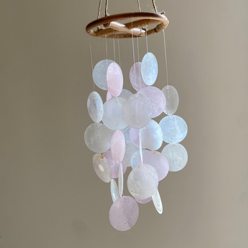 Op de afbeelding: Een windgong van witte en roze schelpen met een houten bovenkant en meerdere hangende schelpen.