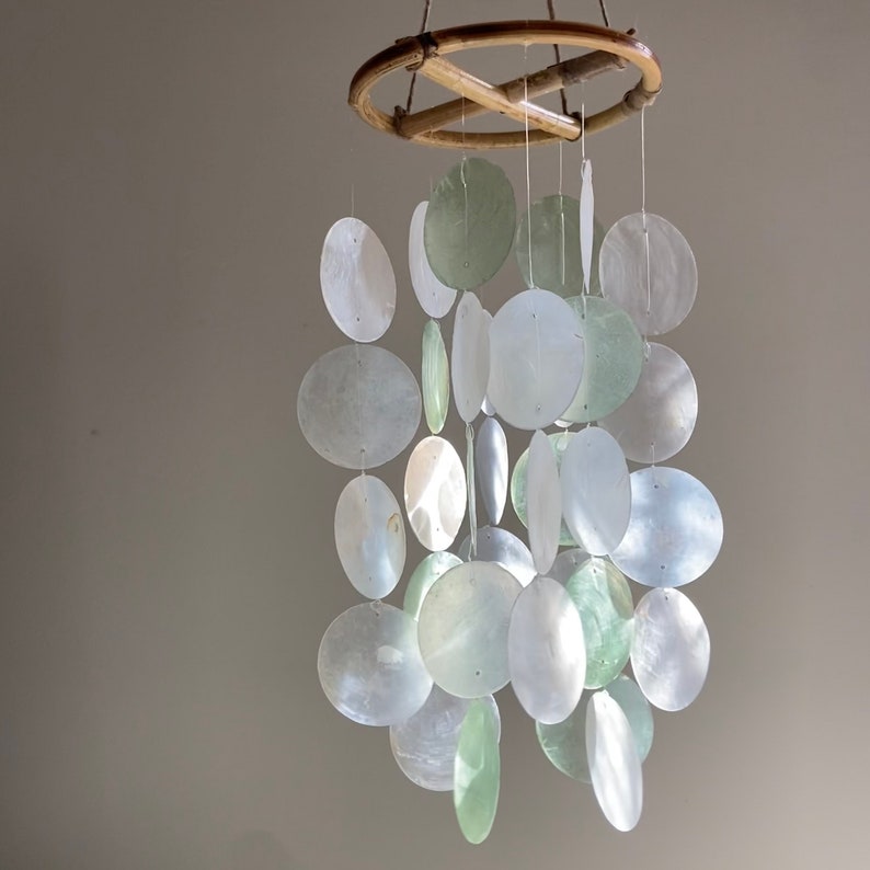 May include: A white and green shell wind chime with a wooden frame. The chime is made of many different sized shells that hang from the frame.