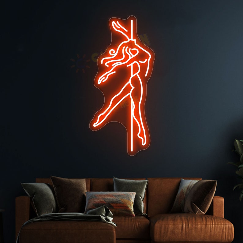 K&ouml;nnte beinhalten: Ein Neon-Schild, das eine Frau in Silhouette zeigt, die an einer Stange tanzt. Das Schild leuchtet in einem leuchtenden Orange und ist an einer dunklen Wand montiert.