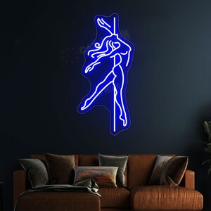 K&ouml;nnte beinhalten: Blaues Neon-Schild, das eine Frau darstellt, die an einer Stange tanzt. Das Schild ist an einer dunkelblauen Wand &uuml;ber einem braunen Sofa angebracht.