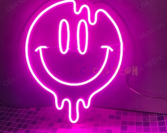 May include: Pink neon light shaped like a dripping smiley face. The light is on and glowing.