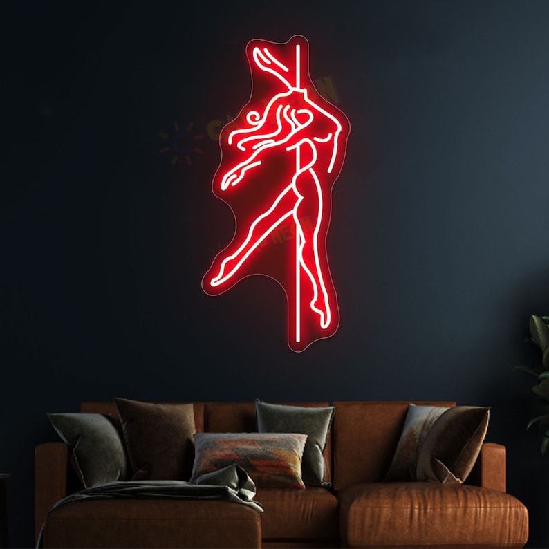 K&ouml;nnte beinhalten: Rotes Neon-Schild, das eine Frau darstellt, die an einer Stange tanzt. Das Schild ist an einer dunklen Wand &uuml;ber einem braunen Sofa angebracht.
