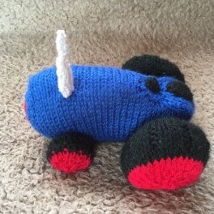 May include: A blue knitted toy tractor with black wheels and red wheel rims. The tractor has a white antenna on the back.