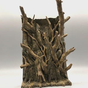 May include: A rectangular, upright display stand featuring a textured, bark-like surface. The front is adorned with multiple protruding, branch-like structures in shades of brown and grey, creating a layered, organic appearance for display.