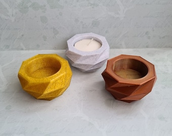 May include: Three geometric candle holders, one white, one gold, and one brown. The white candle holder has a small white candle inside.