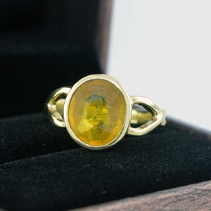 Può includere: Un anello d'oro con una grande pietra ovale di ambra incastonata in una fascia delicata e attorcigliata.