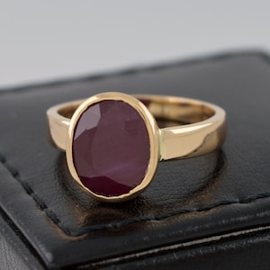 Può includere: Un anello d'oro con una grande pietra preziosa di rubino di forma ovale. L'anello è posto su una scatola di velluto nero.