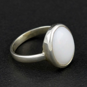 May include: A silver ring with a white oval-shaped gemstone.