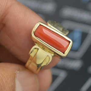 May include: A gold ring with a rectangular, orange coral stone.