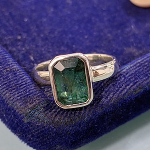 May include: A silver ring with a green emerald-cut gemstone set in a bezel setting.