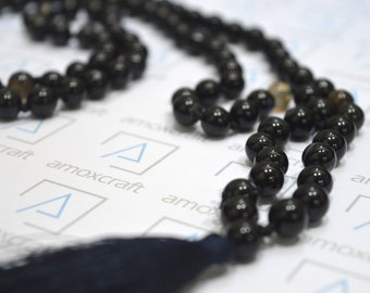 May include: A black beaded necklace with a tassel. The beads are round and smooth, and the tassel is made of a dark fabric.