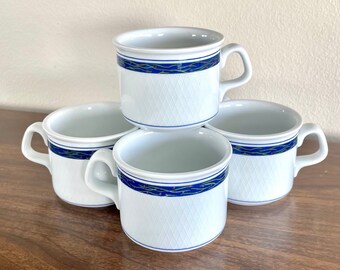 May include: Four white ceramic coffee mugs with blue and green trim. The mugs have a diamond pattern on the sides.
