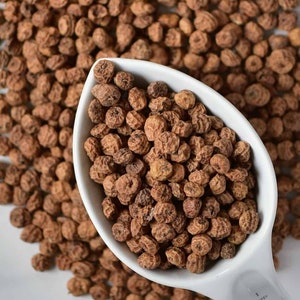 May include: A white measuring cup filled with brown tiger nuts. The cup is sitting on a white surface surrounded by more tiger nuts.