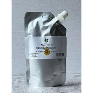May include: A silver pouch of tiger nut oil with a white label. The label has the text "Tiger nut oil" and a small graphic of a drop of oil. The pouch has a white spout and cap.
